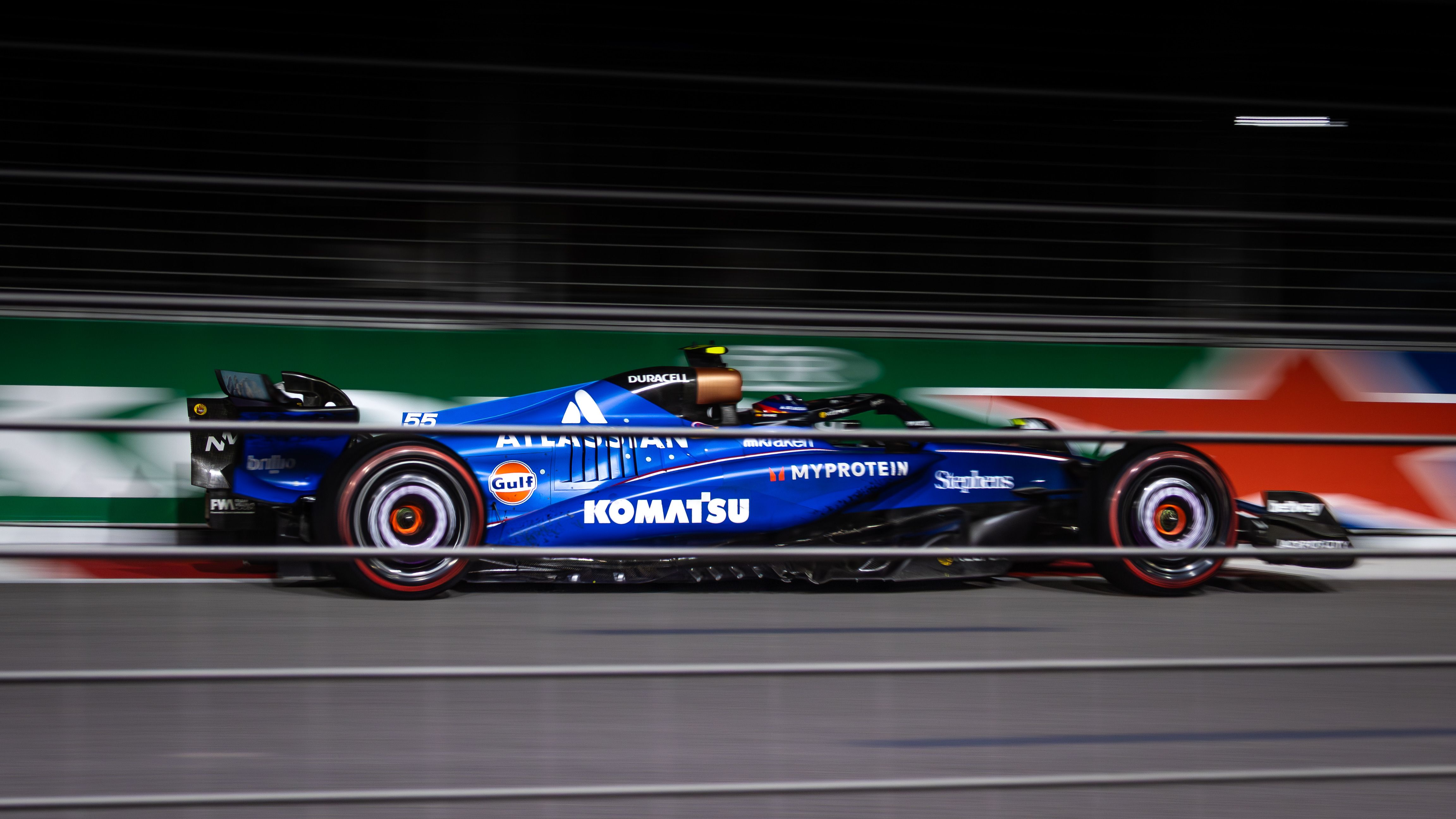 Blue Formula car speeding under floodlights during a night race grand prix