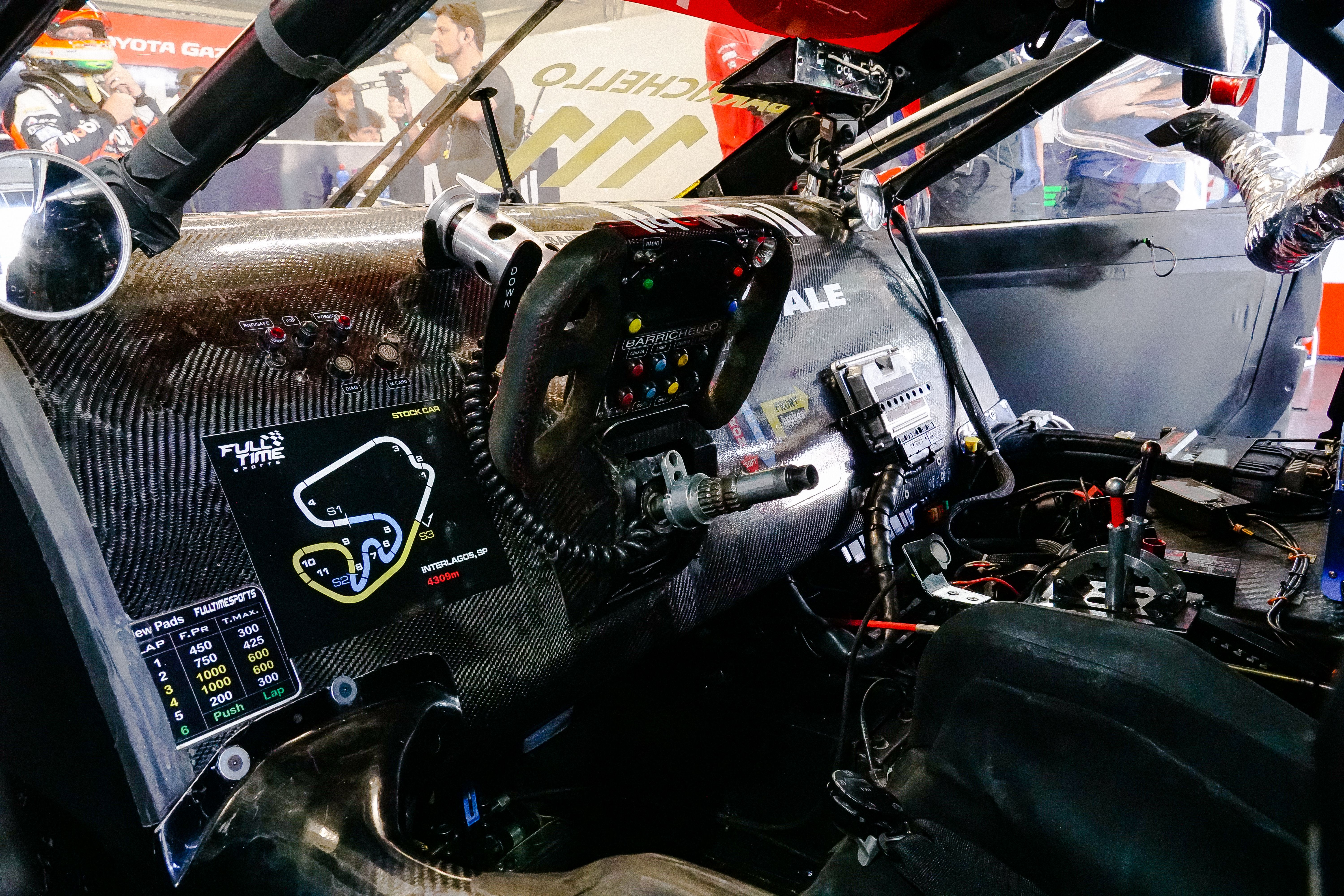 Detailed view of a racing car cockpit showing the carbon fiber dashboard and steering wheel, representing driver controls and car technology